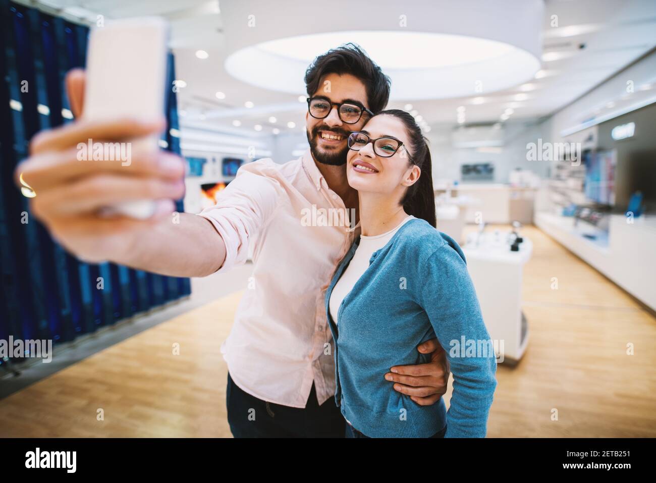 Adorabile giovane coppia sta prendendo un selfie in un negozio di tecnologia molto luminoso. Foto Stock