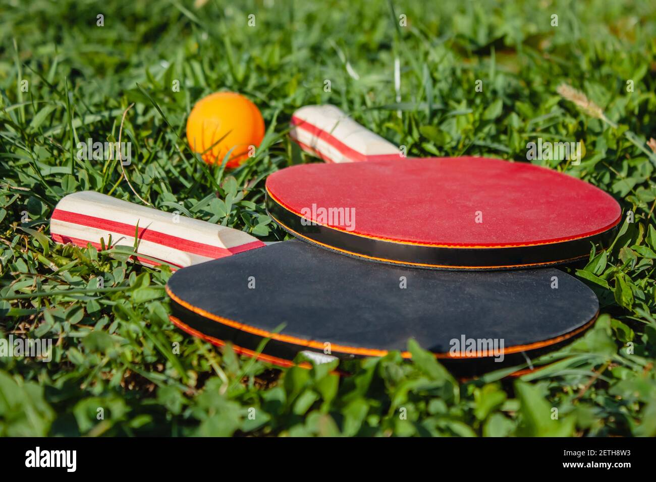 Due racchette da ping pong e una palla arancione giacciono sull'erba. Il concetto di giochi sportivi all'aperto Foto Stock