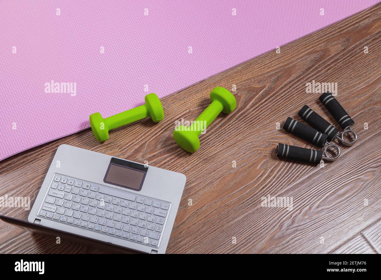 Tappetino fitness, manubri, espansore e laptop per allenamenti online a casa. Concetto di apprendimento online in relazione alla pandemia Foto Stock