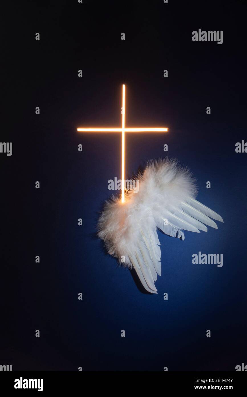 Le ali bianche sono lasciate accanto ad una croce brillante. Temi religiosi. Messa a fuoco selettiva, esposizione lunga. Foto Stock