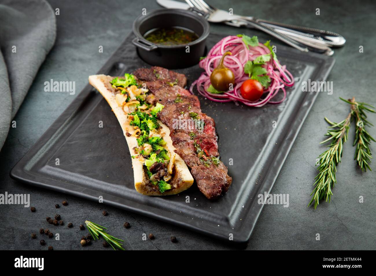 bistecca di manzo con osso zuccherino, servita con salsa e insalata di cipolle, pomilori e peperoni. sfondo scuro Foto Stock