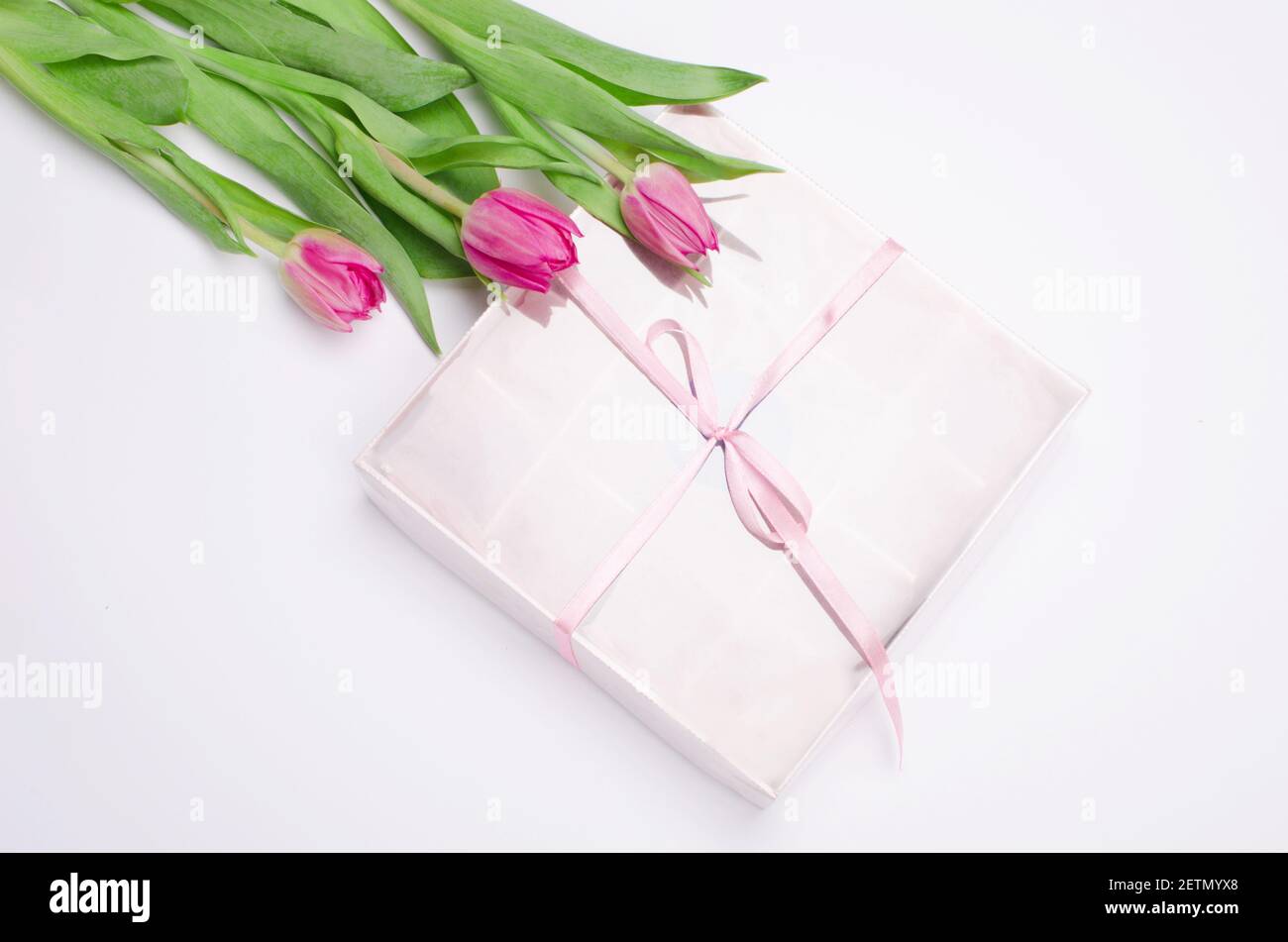 Confezione regalo con cuori di dolci al cioccolato e tulipani su sfondo bianco. Deserto per San Valentino Foto Stock