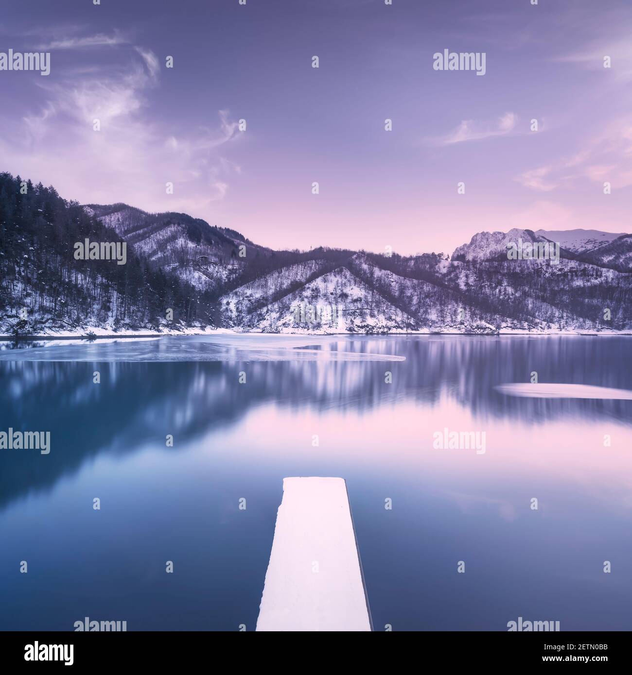 Lago ghiacciato e molo innevato nelle montagne Apuane in inverno. Garfagnana, Toscana, Italia, Europa. Fotografia a lunga esposizione. Foto Stock
