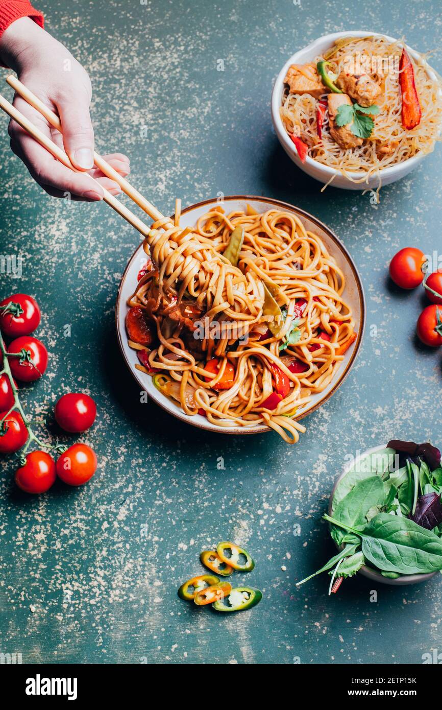 primo piano su un piatto di noodle cinesi che si avvolge a mano tagliatelle su bastoncini accanto ai pomodori al basilico su sfondo verde Foto Stock