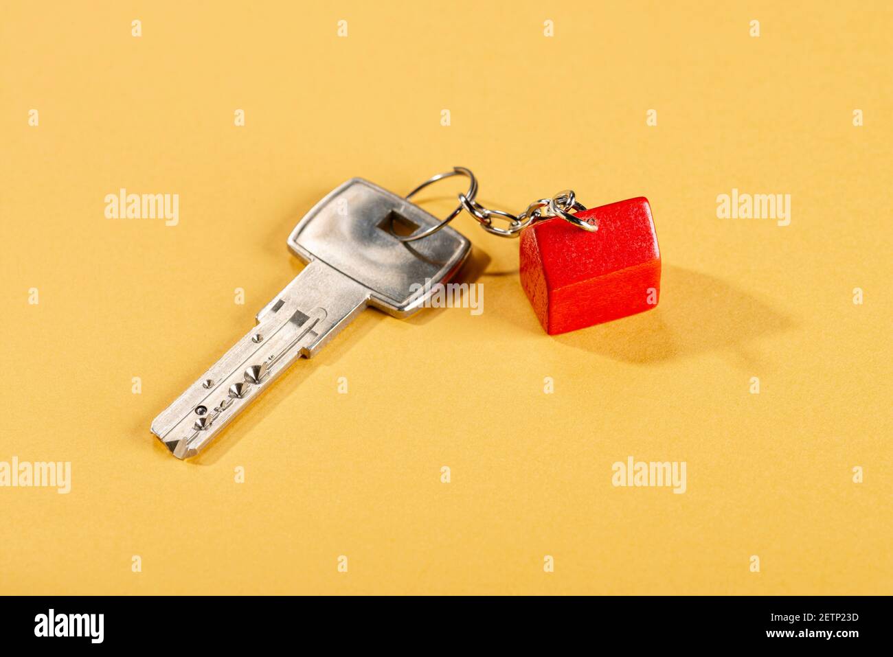 Chiave con una piccola casa rossa come chiave elettronica su sfondo giallo Foto Stock