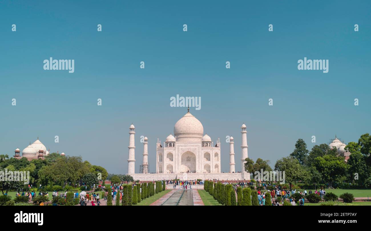 Vista frontale del bellissimo Taj Mahal fiancheggiato da alberi con foglie verdi e pochi visitatori in una luminosa mattina estiva ad Agra, India. Foto Stock