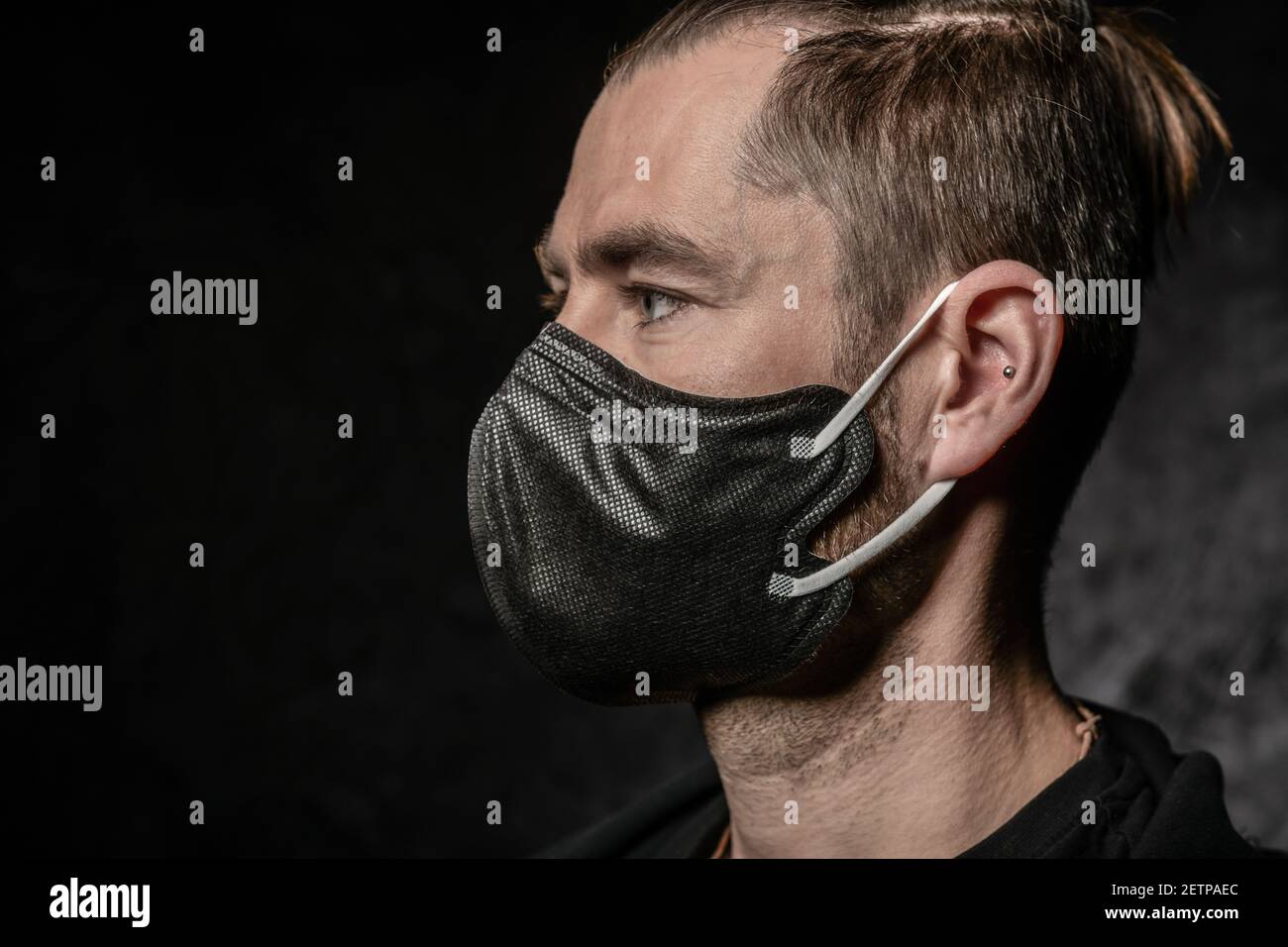 Un uomo con maschera nera sul viso uno sfondo scuro nello studio Foto Stock
