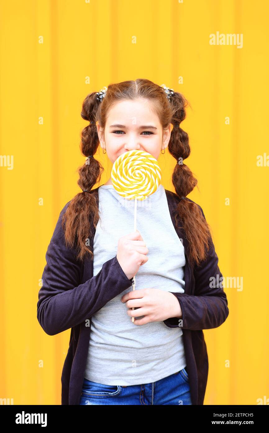 Ragazza con una caramella grande nelle sue mani su uno sfondo giallo. Foto Stock