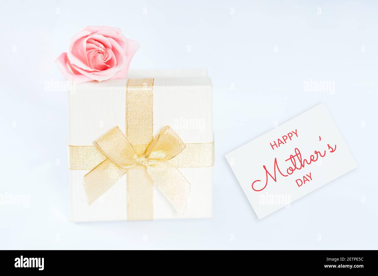 Scatola bianca con regalo all'interno avvolto in nastro d'oro con abow, sulla scatola si trova rosa davanti a sfondo bianco. Festa regalo San Valentino, 14 Foto Stock