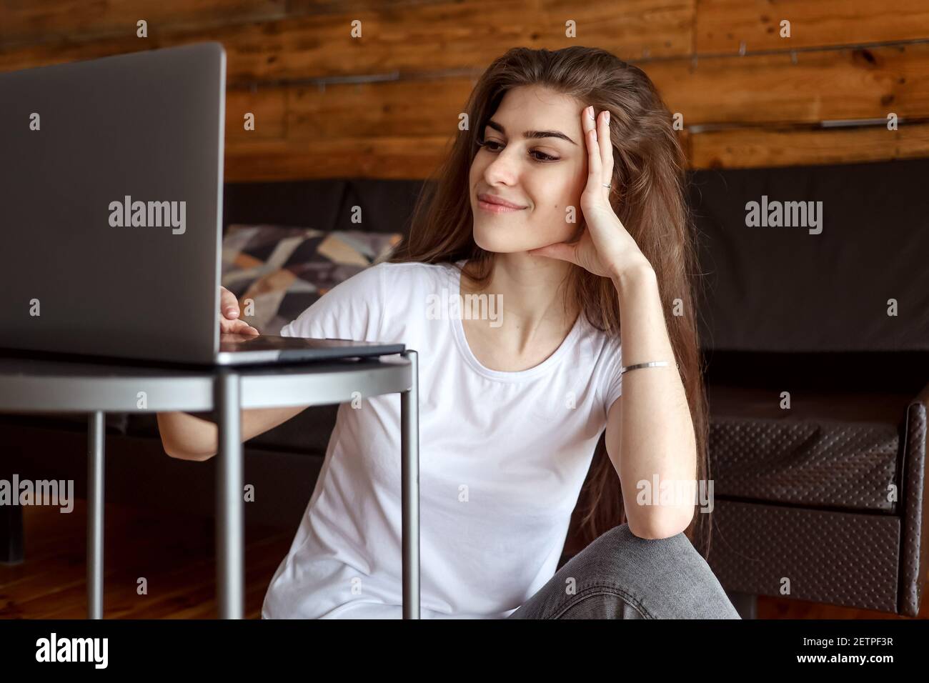 Attraente studente di ragazza sorridente felice che ha videochat seduto sul pavimento, utilizzando un computer portatile. Bella donna ama guardare il webinar educativo Foto Stock