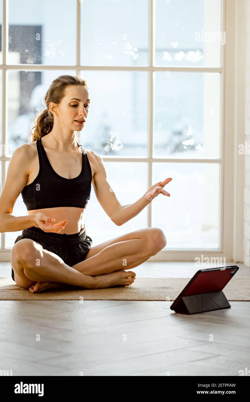 Insegnante di yoga che conduce una lezione di yoga virtuale a casa in una videoconferenza. Bella donna in forma che pratica yoga online con tablet. Fitness e wor domestici Foto Stock