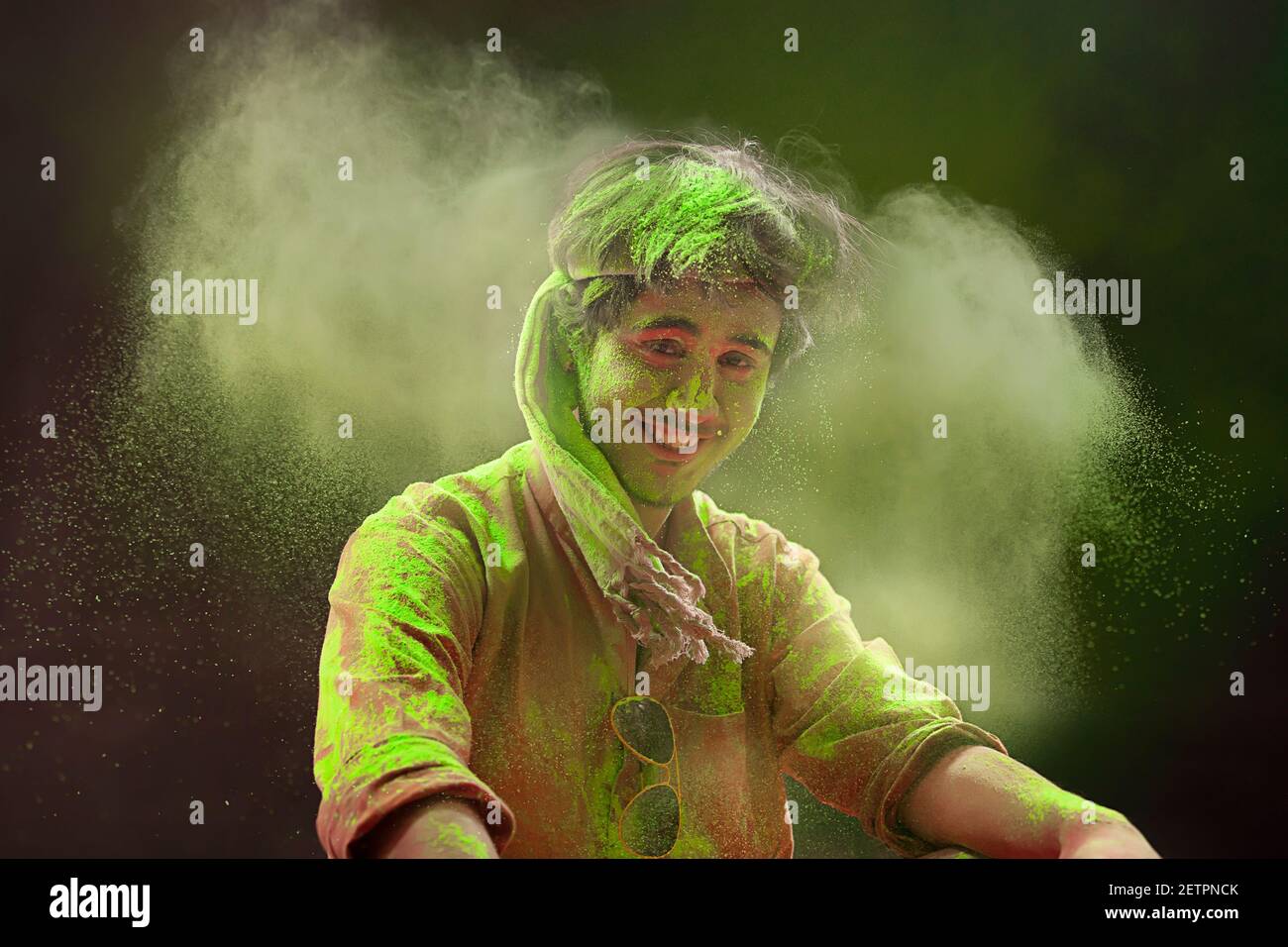 UN GIOVANE SEDUTO INTORNO A COLORI HOLI GUARDANDO LA MACCHINA FOTOGRAFICA E SORRIDENDO Foto Stock