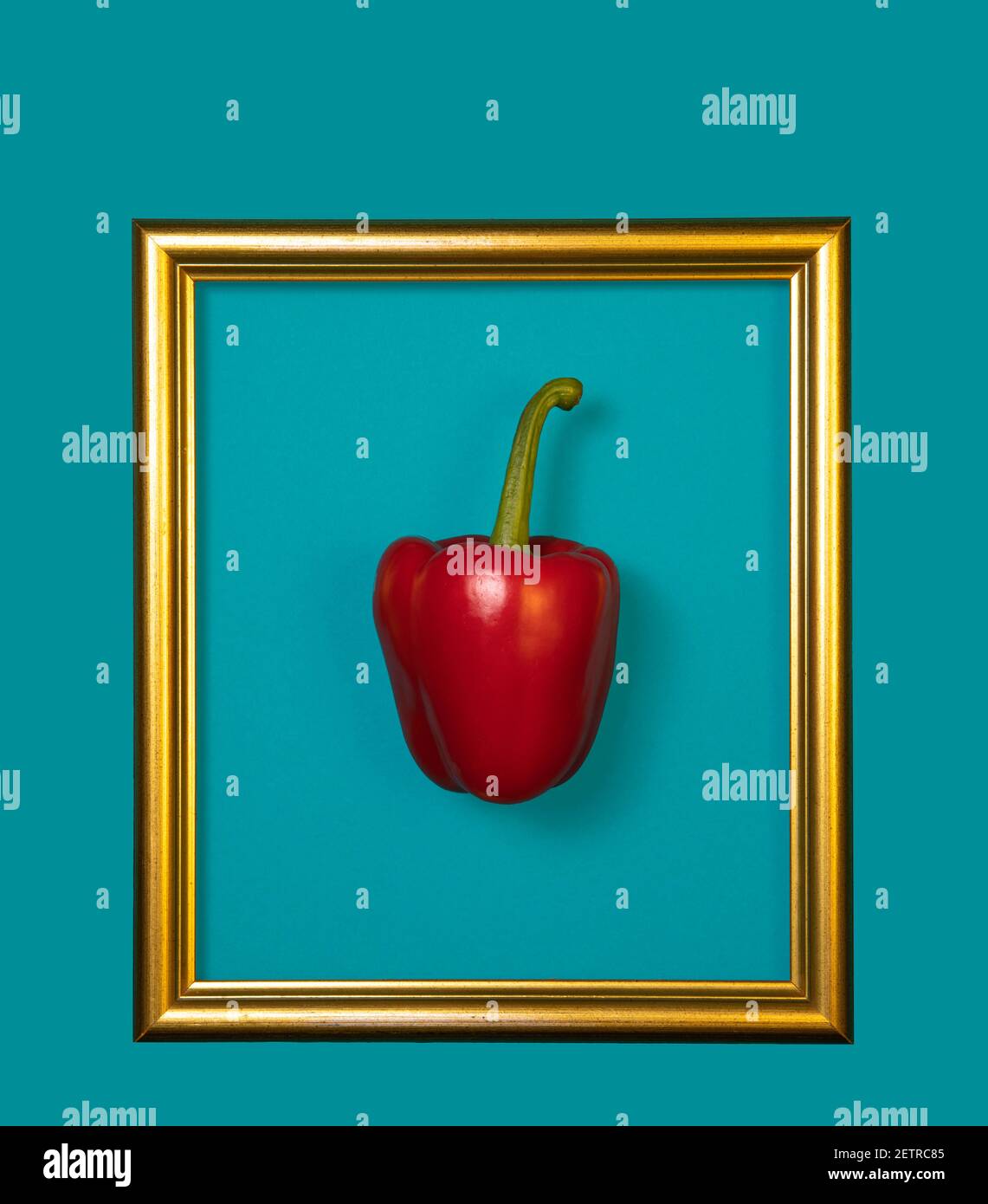 Peperone rosso con cornice dorata. Concetto minimo di posa piatta, con sfondo blu. Dieta sana Foto Stock