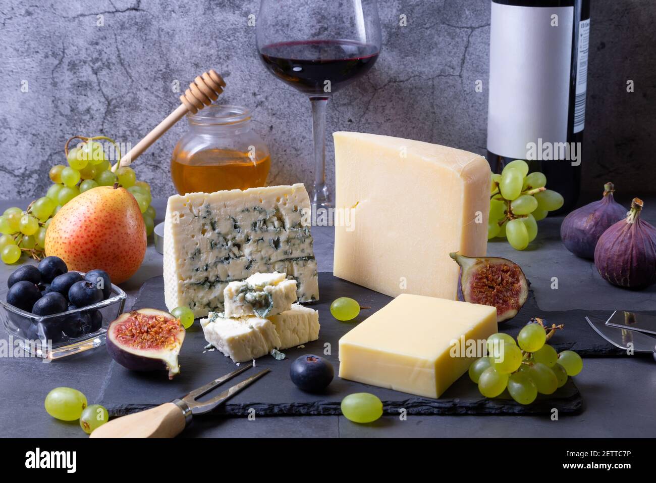 Formaggio blu e parmigiano su tavola nera, frutta, vino e miele. Primo piano. Foto Stock