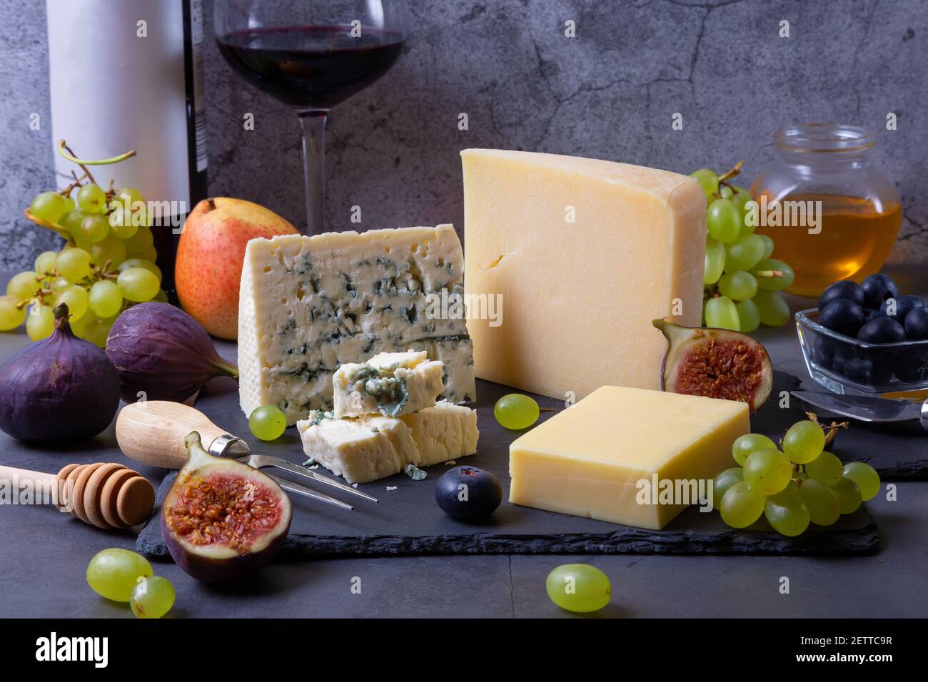 Formaggio blu e parmigiano su tavola nera, frutta, vino e miele. Primo piano. Foto Stock