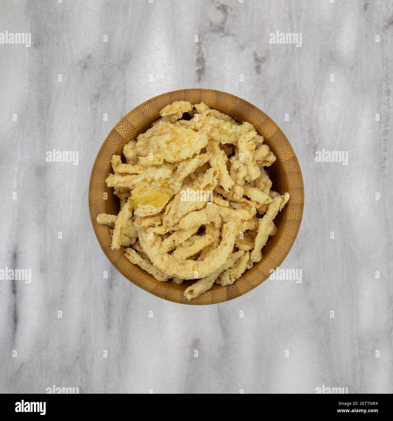 Vista dall'alto di una piccola ciotola di legno riempita con cipolle fritte impanate su un piano di marmo. Foto Stock