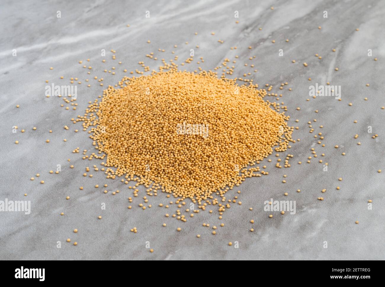 Vista laterale di un mucchio di semi di amaranto organico con alcuni sparsi su un piano di marmo grigio illuminato con luce naturale. Foto Stock