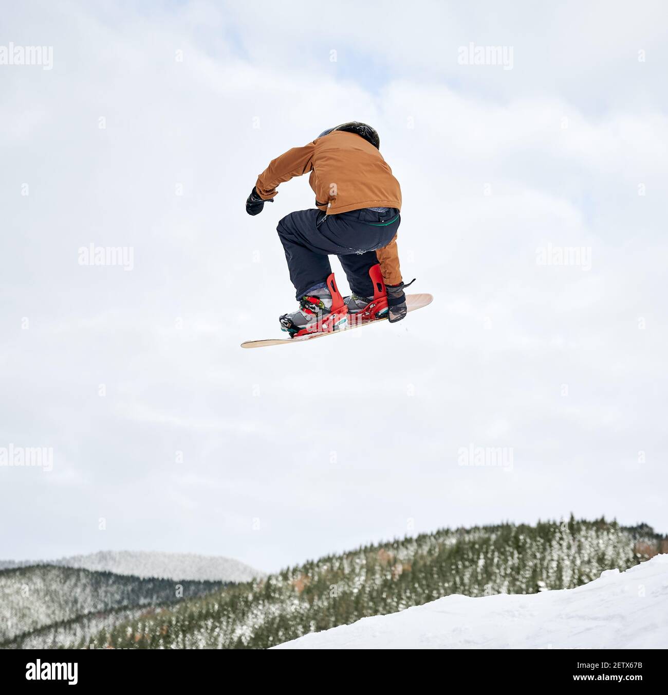 Vista posteriore dello snowboarder ragazzo in giacca invernale e casco che salta in aria. Adorabile bambino che fa saltare con snowboard mentre scivola giù collina innevata nelle montagne invernali. Concetto di sport invernale estremo Foto Stock