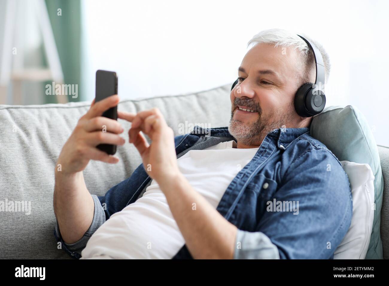 Allegro uomo con capelli grigi in cuffia che ascolta la musica sul telefono Foto Stock