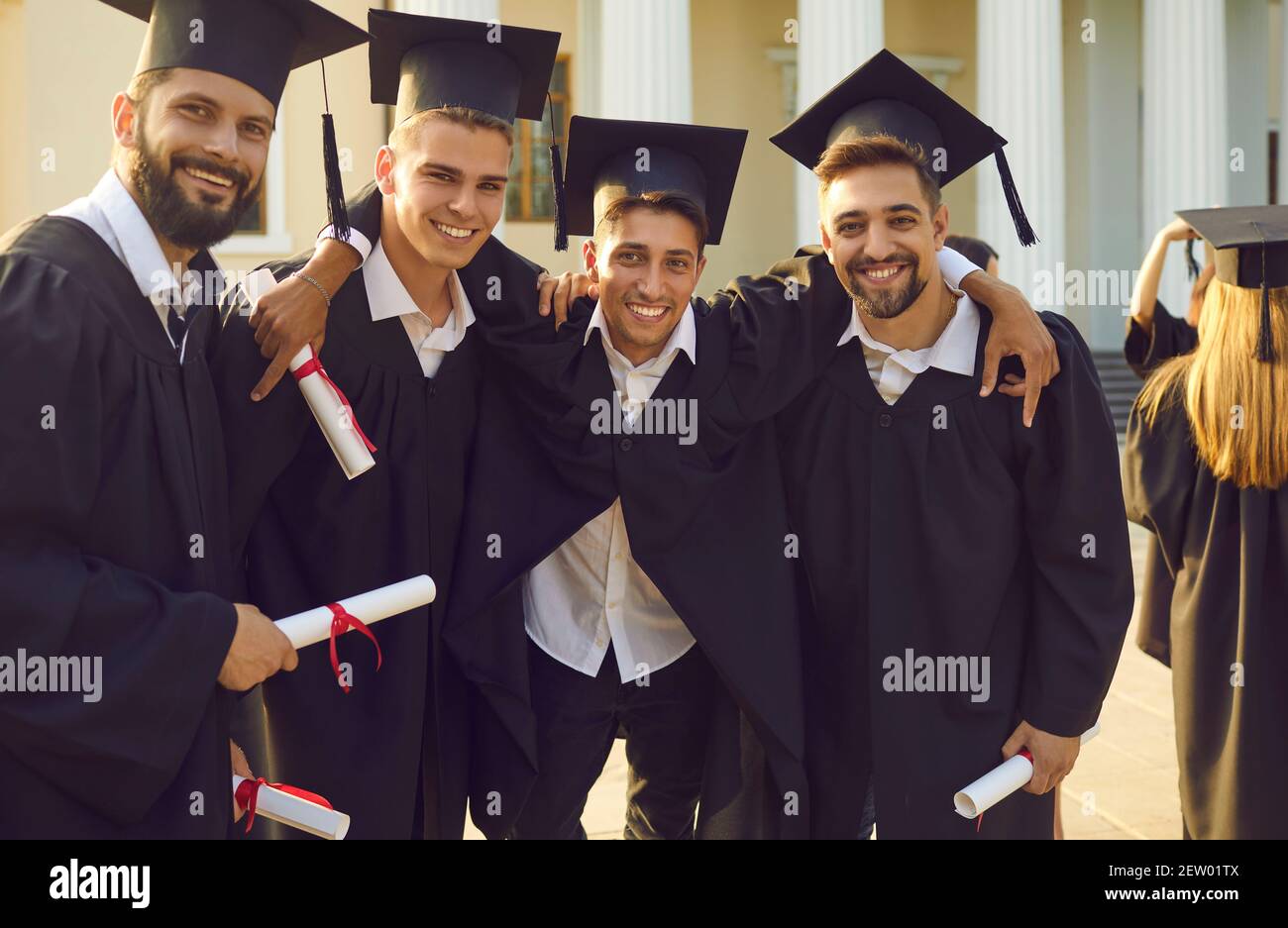 Uomini sorridenti studenti universitari laureati in piedi, abbracciando e festeggiando ottenere diplomi Foto Stock
