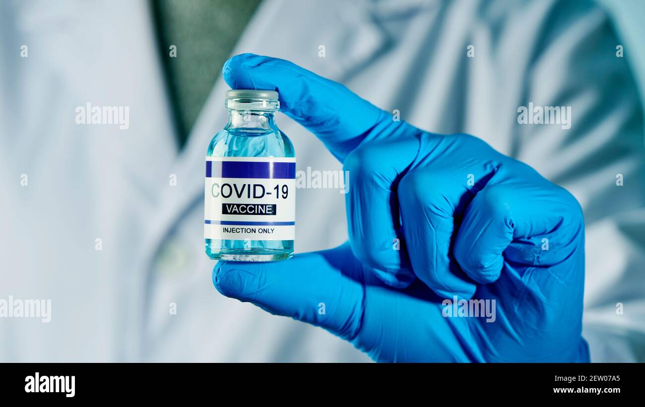 closeup di un operatore sanitario, indossando guanti chirurgici blu, con una bottiglia vaccinale covid-19 simulata in mano Foto Stock