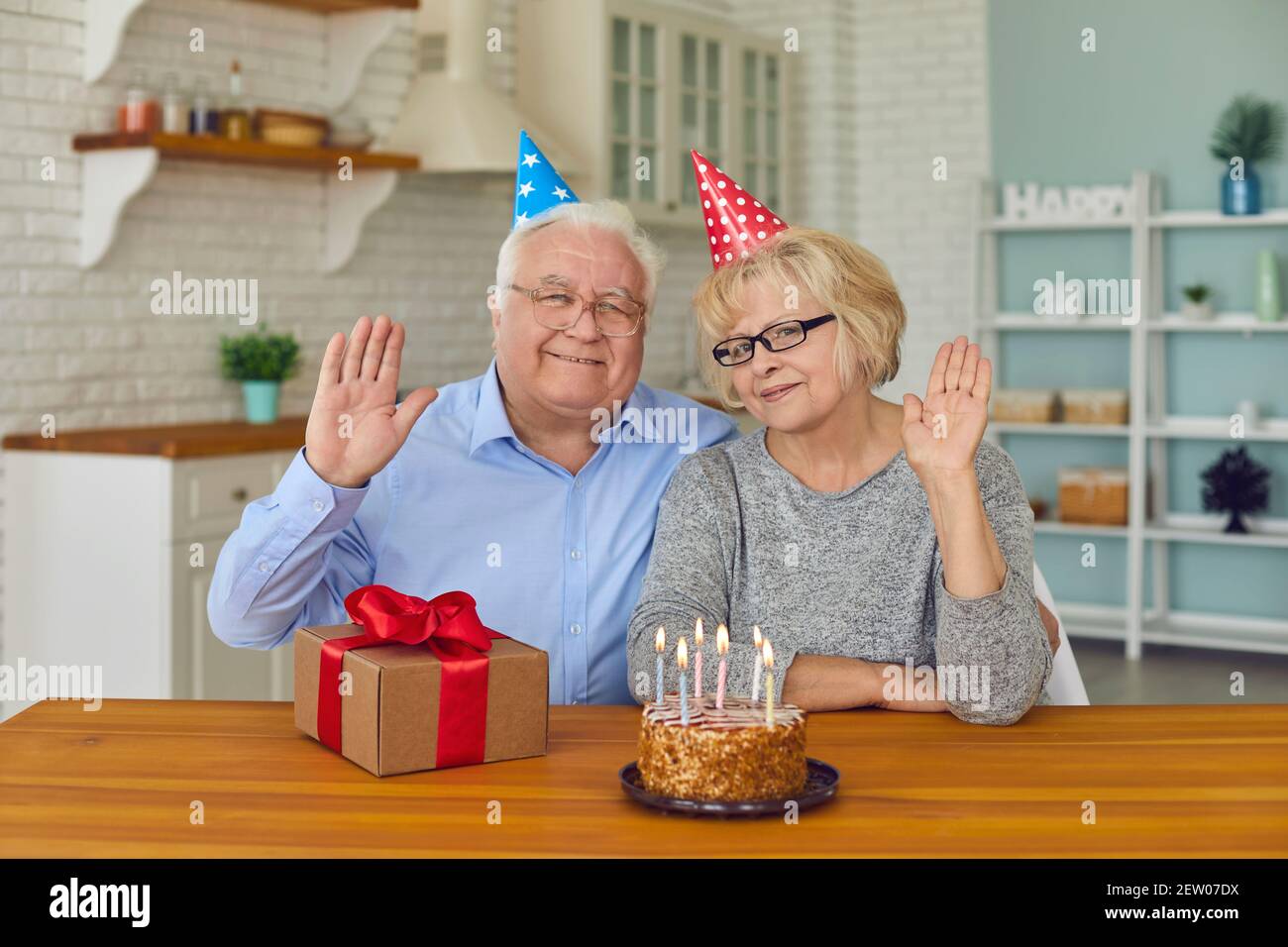 Felice coppia ritirata in cappelli festosi seduti con torta di compleanno e presenta la scatola Foto Stock