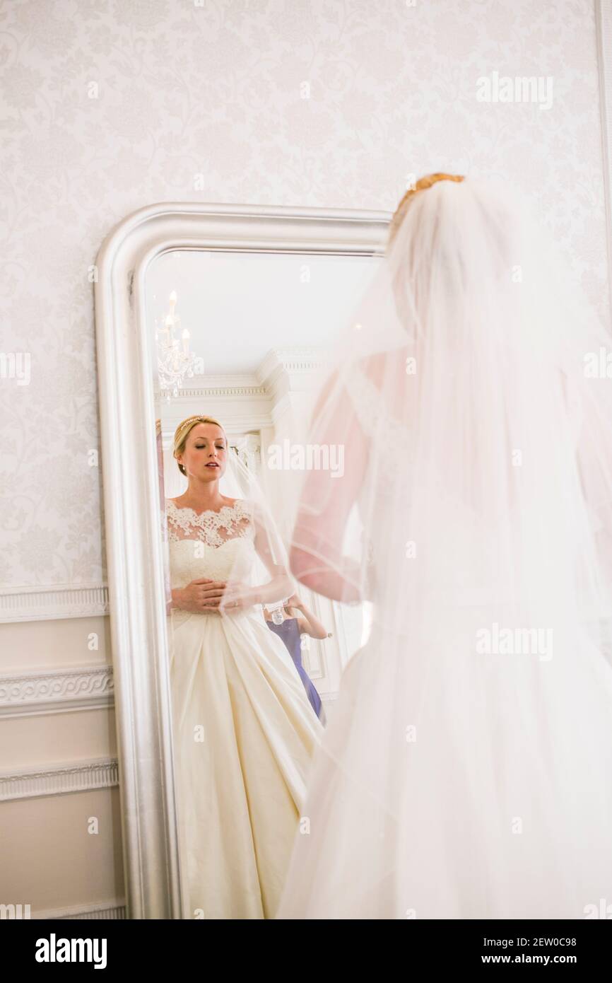 Sposa che si prepara il suo giorno di nozze. Guarda uno specchio a lunghezza intera. Sta tenendo lo stomaco a causa dell'eccitazione di ansia e dei nervi. Foto Stock