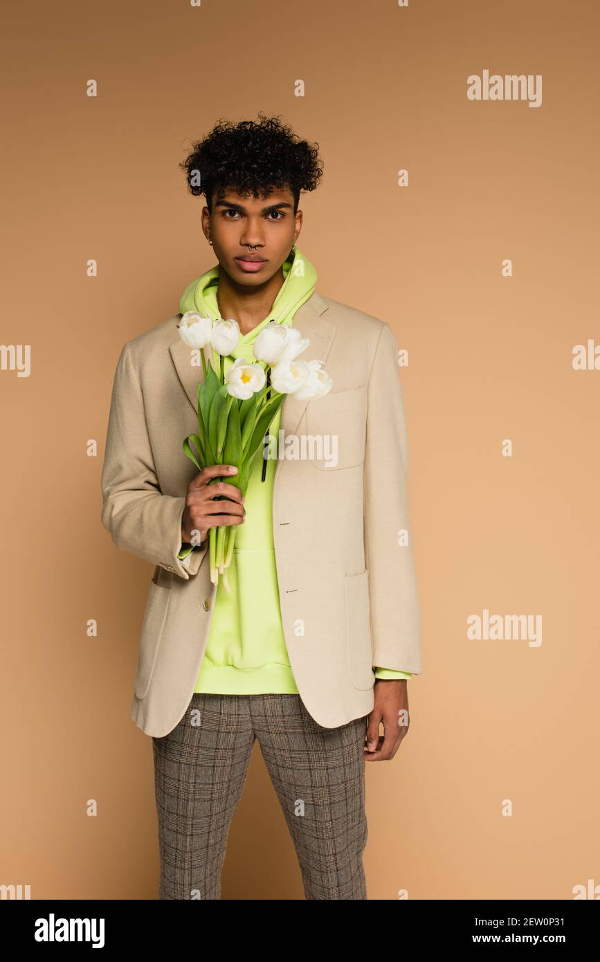 giovane afroamericano in felpa con cappuccio e blazer che tiene tulipani su  beige Foto stock - Alamy