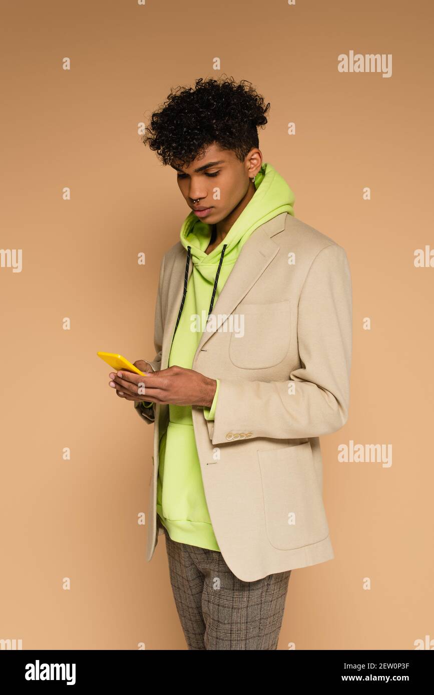 uomo afro-americano trendy in felpa con cappuccio e blazer con smartphone  su beige Foto stock - Alamy