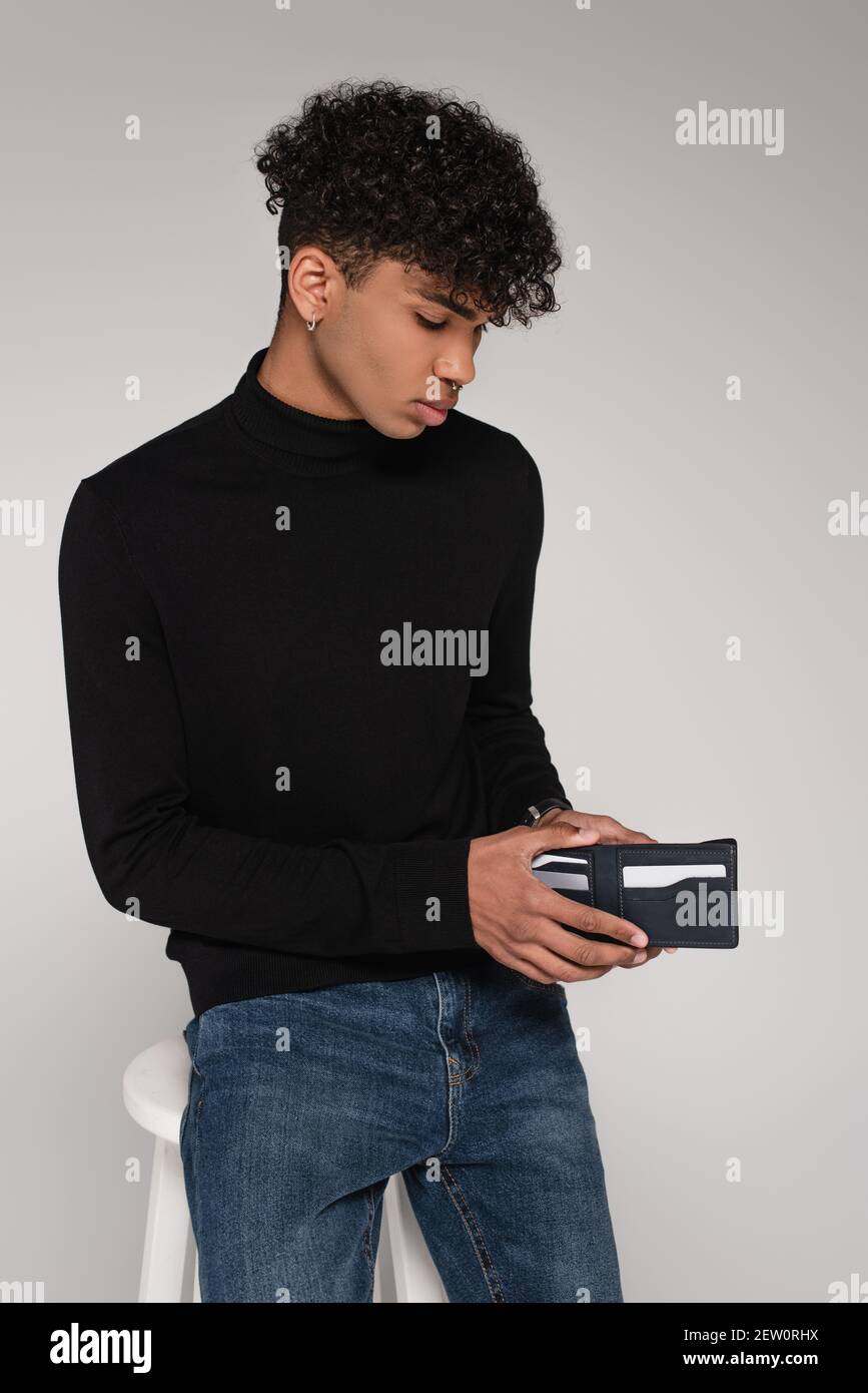 giovane afroamericano guardando all'interno del portafoglio in pelle isolato su grigio Foto Stock