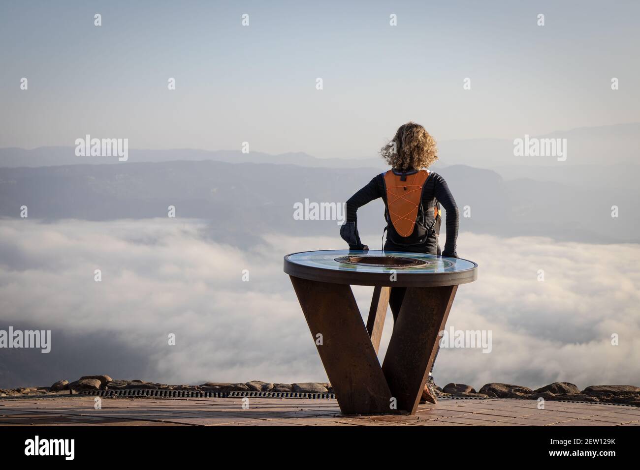 Atleta femminile in piedi su una montagna guardando sopra nuvole spesse Foto Stock