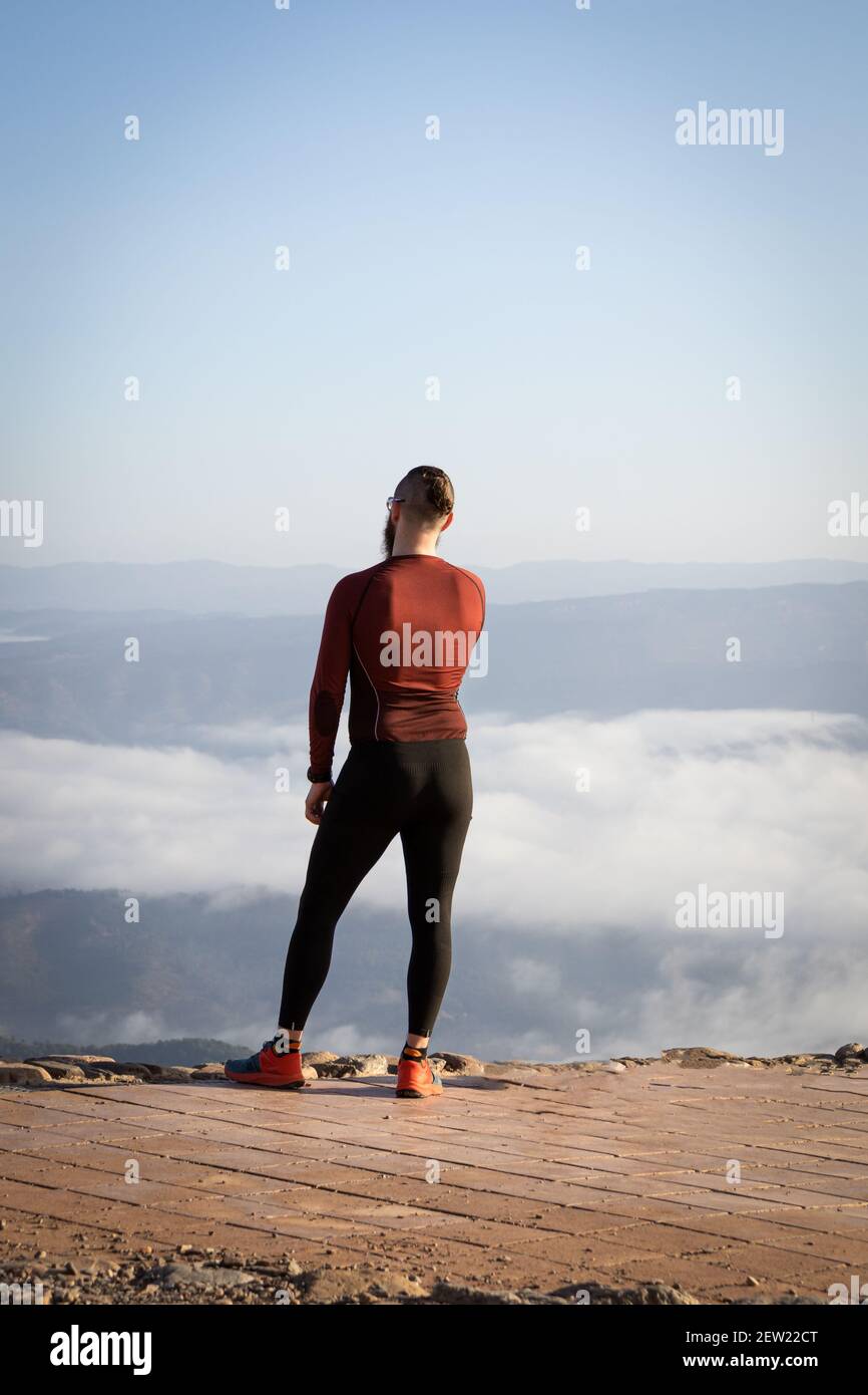 Atleta maschile in piedi su una cima di montagna guardando sopra il nuvole spesse Foto Stock