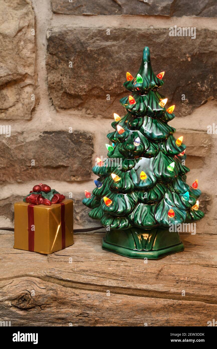 Albero di Natale in ceramica illuminato e candela in scatola regalo su legno manto di fienile su camino di pietra Foto Stock