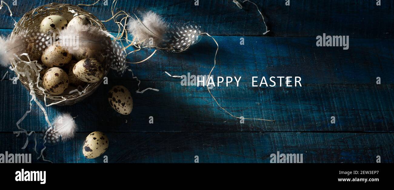 Sfondo della bandiera di Pasqua felice; immagine di stile retro con uova di Pasqua e piume in cestino d'argento su sfondo blu scuro con spazio di copia. Foto Stock