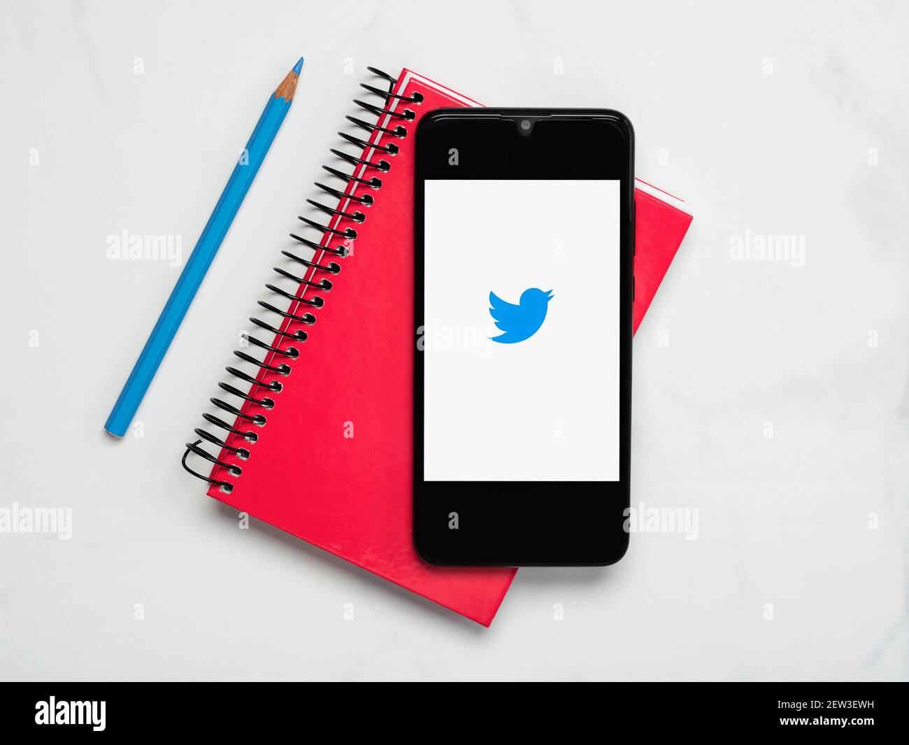 Icona dell'applicazione Twitter sullo schermo bianco dello smartphone con notebook e matita blu su sfondo bianco Foto Stock