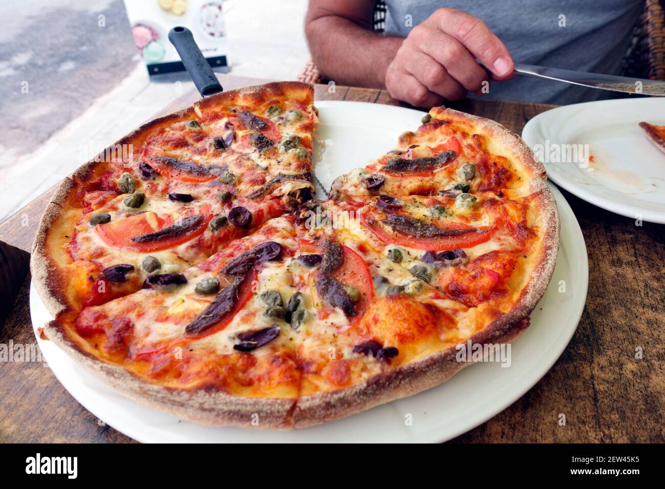 Pizza con acciughe e pomodoro su una lunga pagaia per pizza maneggiata In una taverna greca sull'isola di Kos Foto Stock