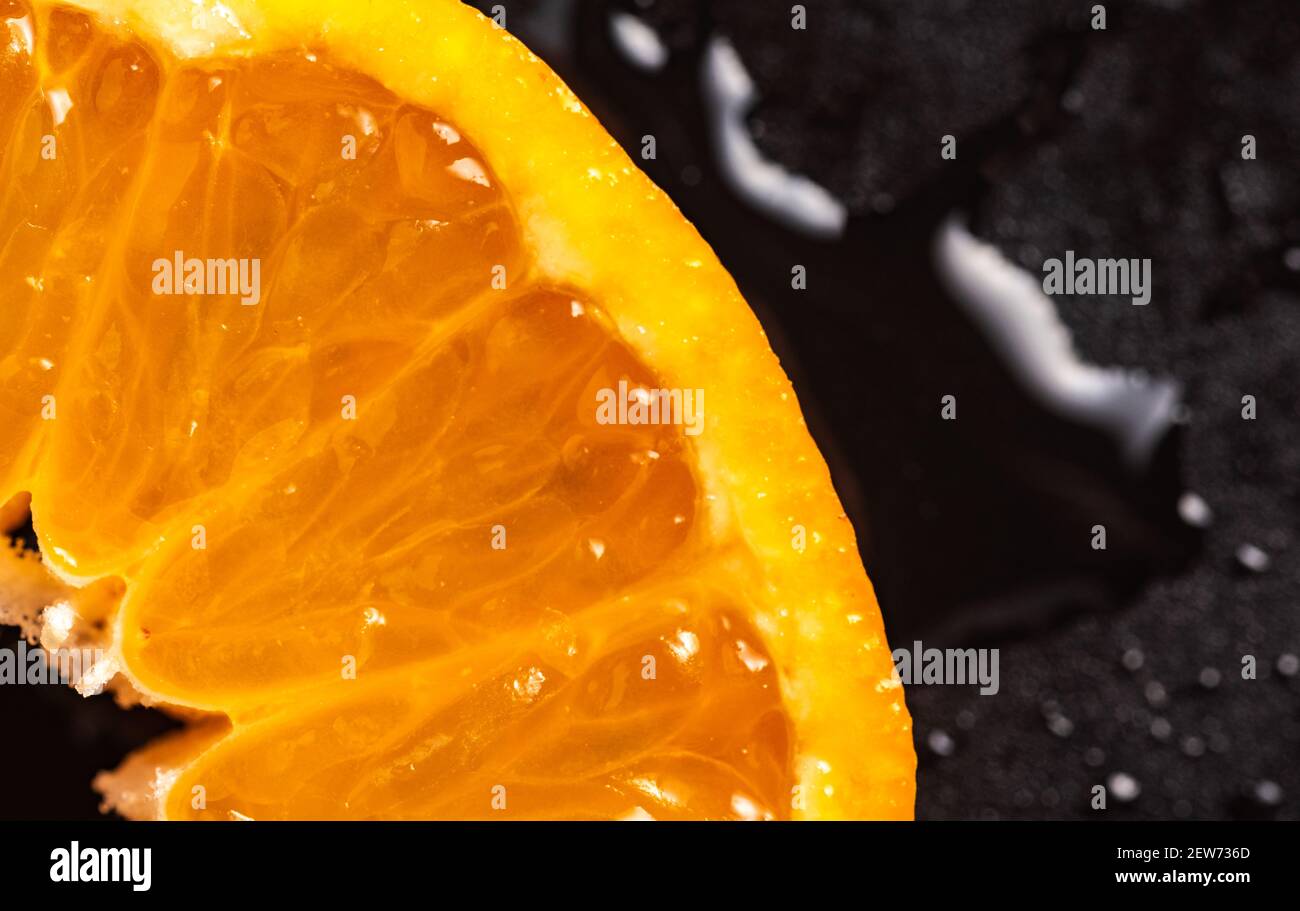 Fetta di mandarino, closup dettagliato su sfondo nero, con gocce d'acqua. Foto Stock