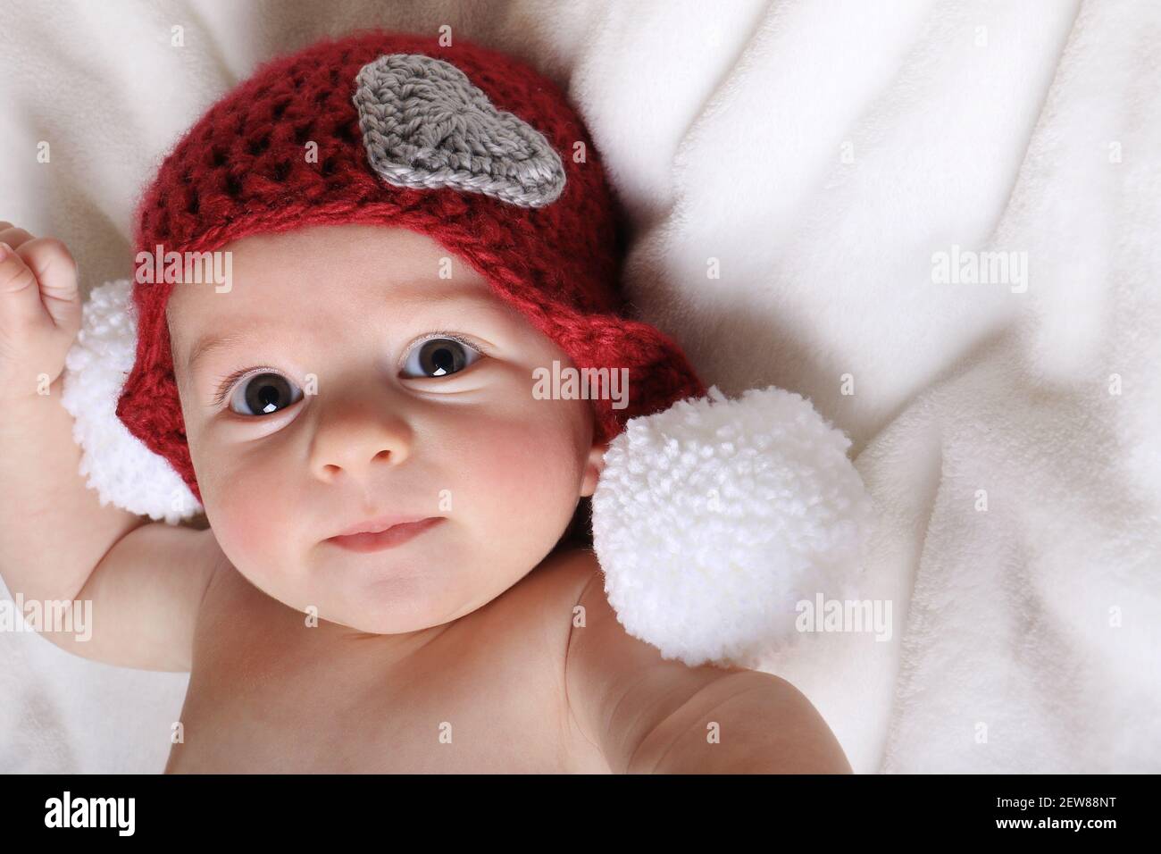 Un neonato di San Valentino che indossa un cappello rosso con un cuore su bianco. Foto Stock
