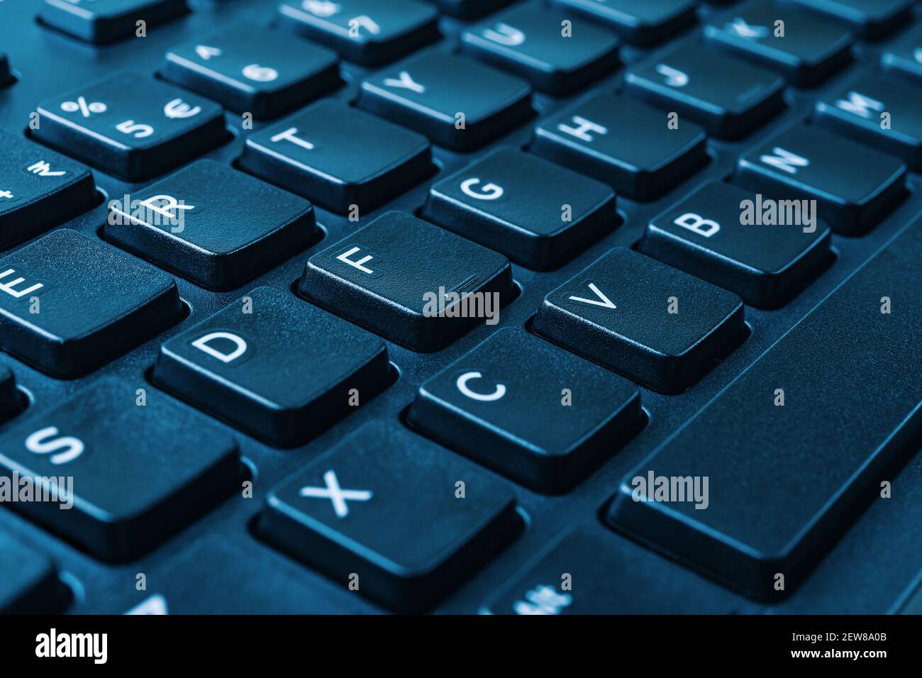 Primo piano della tastiera nera del computer su tono blu. Formazione a distanza, lavoro online, business e shopping, confermare l'ordine dei prodotti o il concetto di accordo Foto Stock