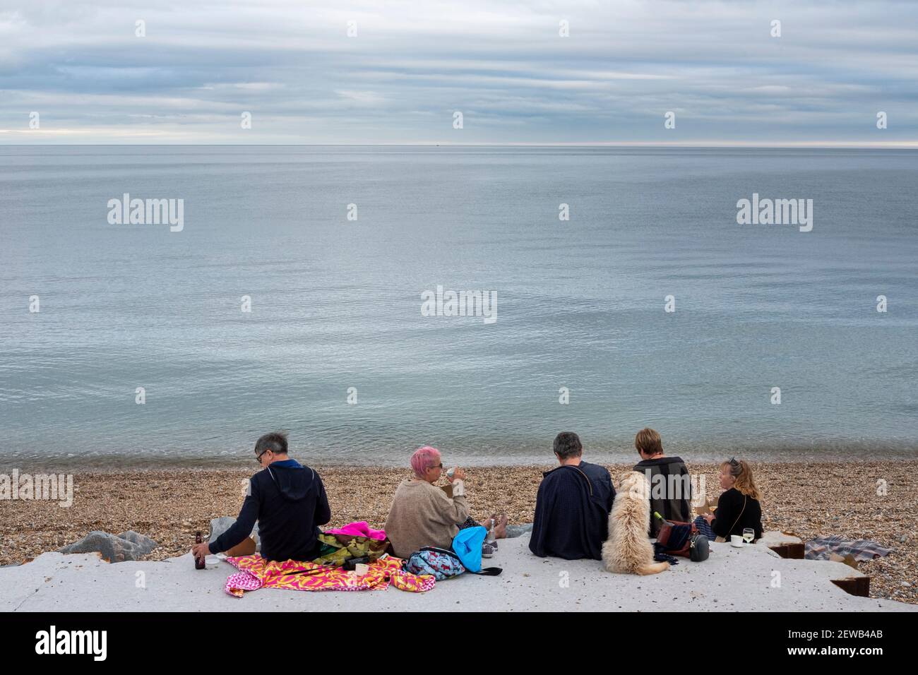 Gruppo di amici che mangiano una cena da picnic sulla spiaggia a Beesands, Devon del sud. Foto Stock