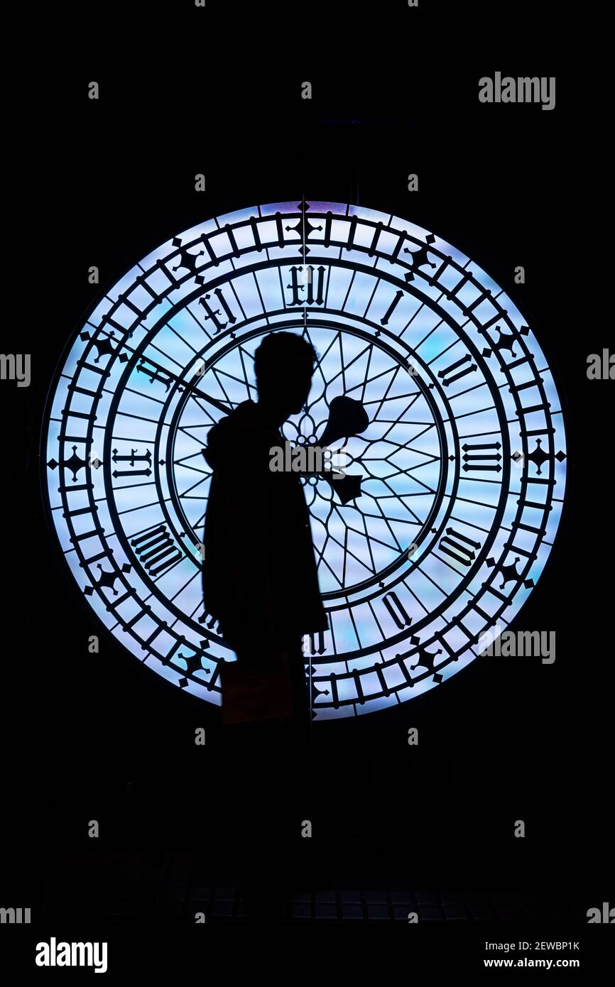 passando il tempo; la silhouette di un uomo che cammina di fronte a un grande orologio vecchio stile di notte Foto Stock