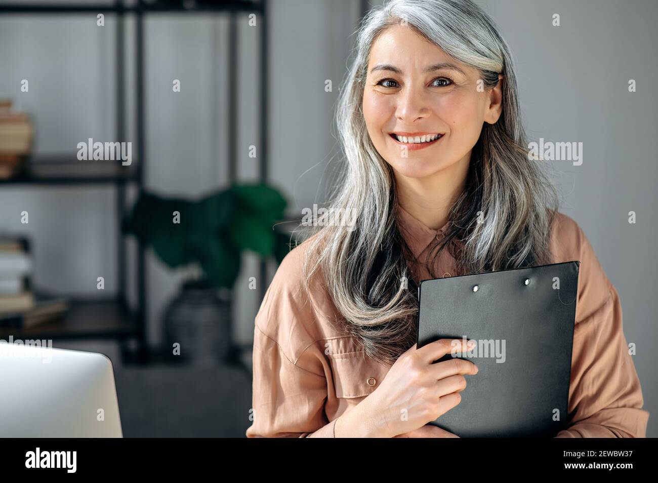 Primo piano ritratto di una donna, una donna o una allenatrice con capelli grigi, in piedi in ufficio, che guarda e sorride amichevole nella fotocamera Foto Stock