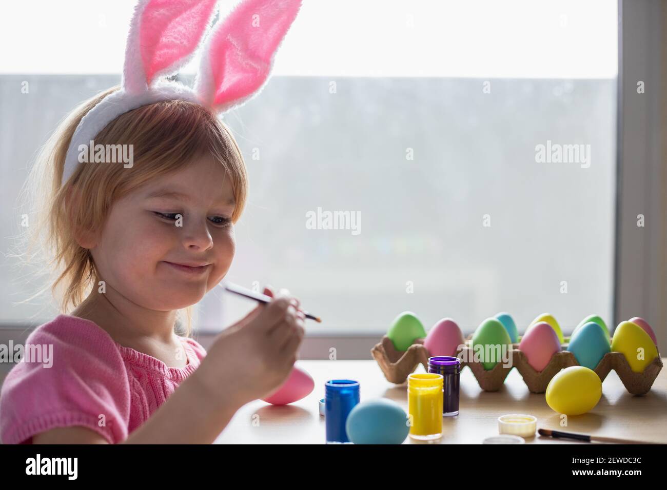 Bambina in orecchie conigliate di Pasqua pittura uova colorate. Festa di Pasqua in famiglia festa a casa e artigianato concetto. Foto Stock