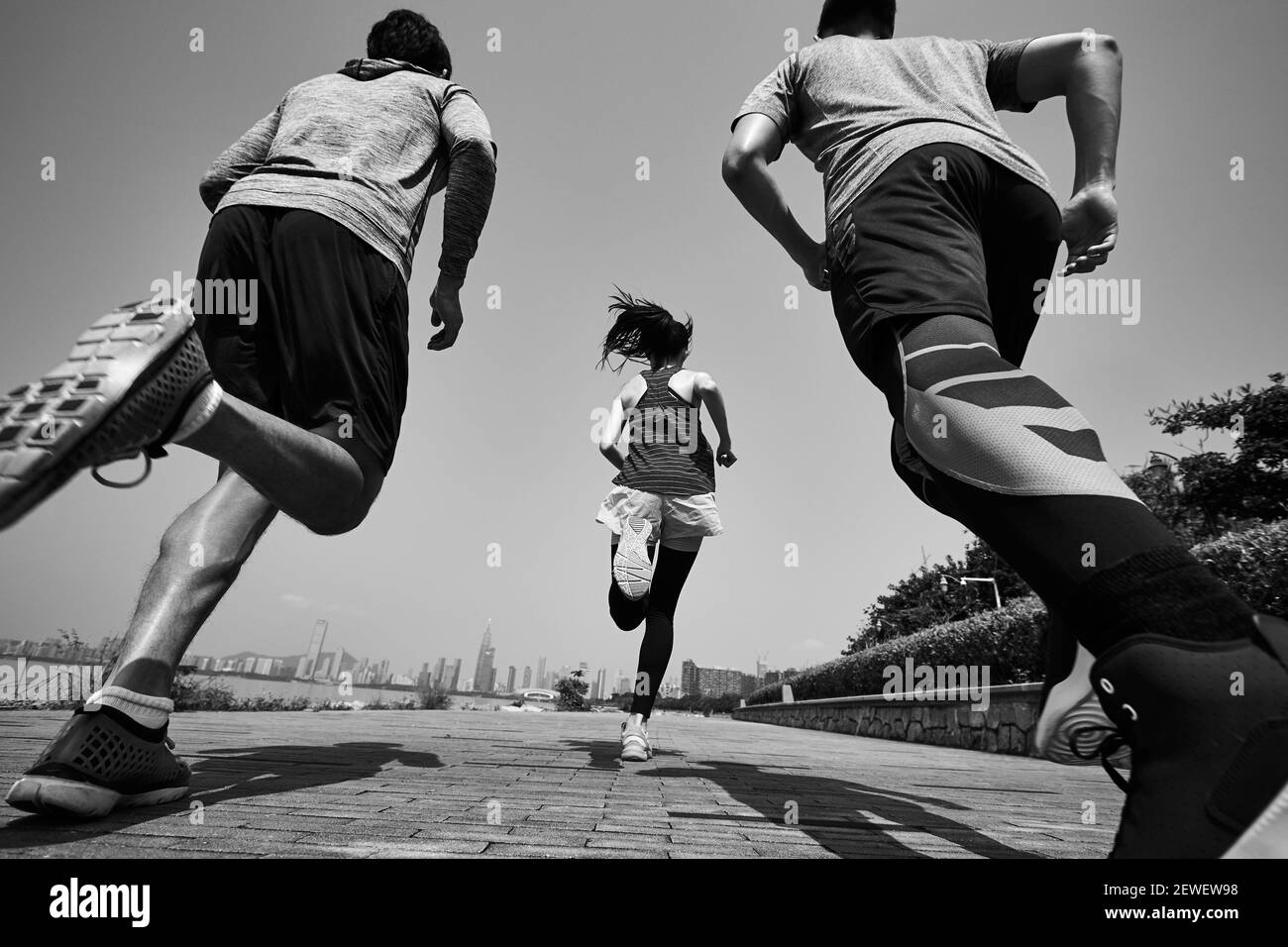 tre giovani adulti asiatici che corrono all'aperto, vista posteriore e ad angolo basso, in bianco e nero Foto Stock