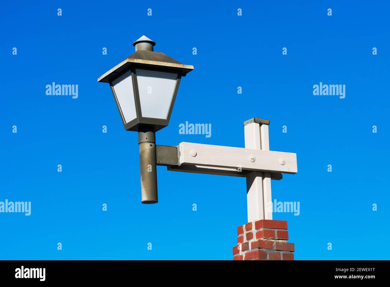 Lampada decorativa con testa lanterna e vetro bianco su palo in legno e base in mattoni. Cielo blu. Foto Stock