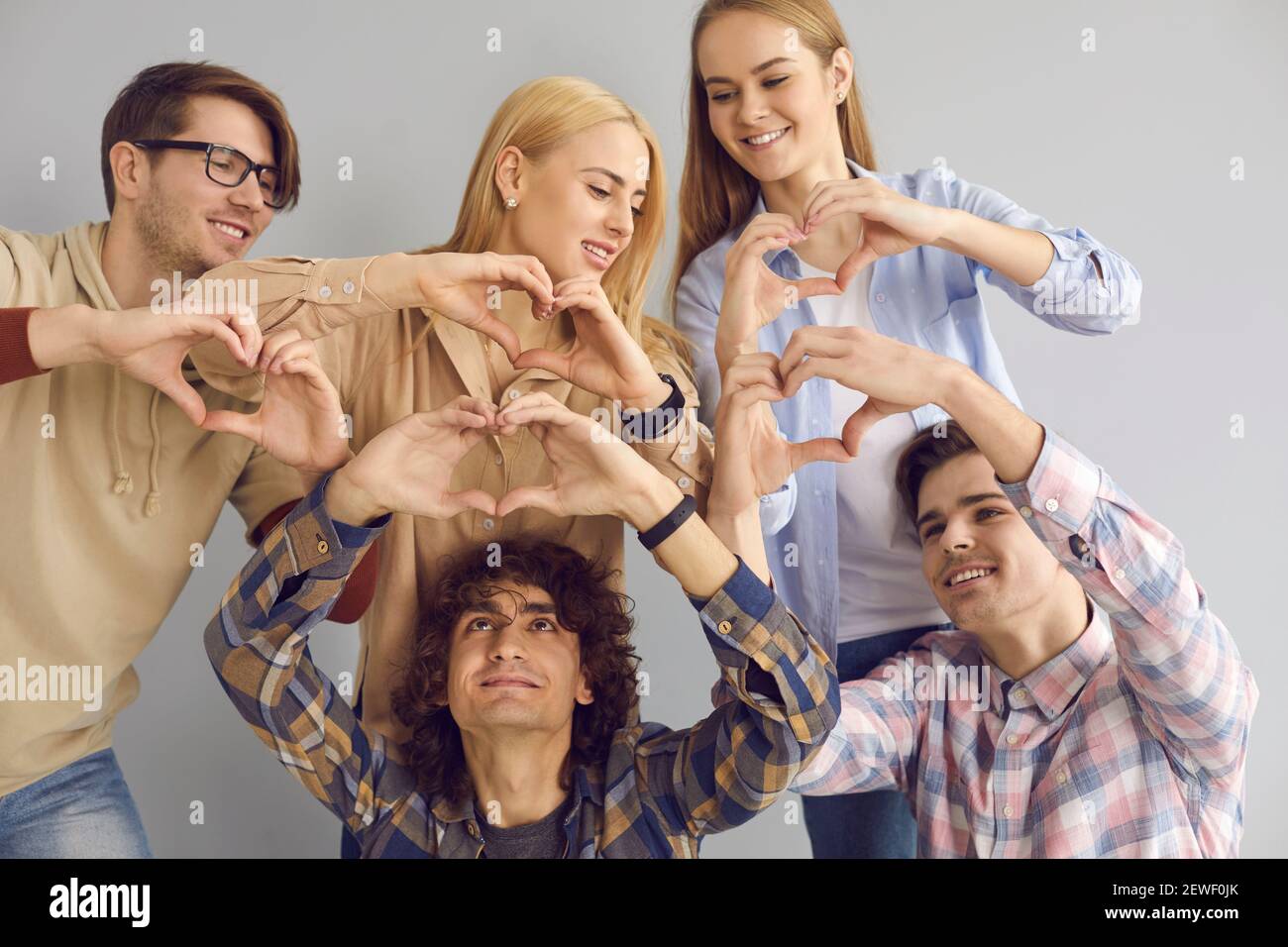 Gruppo di giovani felici e grati che fanno la forma simbolica del cuore gesti insieme Foto Stock