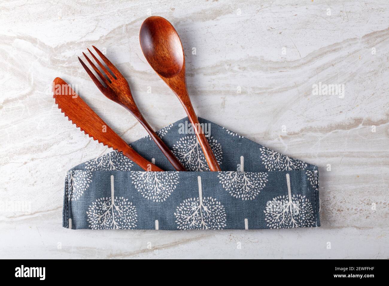 Primo piano immagine piatta isolata di un set di posate in legno composto da un cucchiaio per zuppa, una forchetta per insalata e un coltello da tavola che si stacca da un fabri decorativo Foto Stock