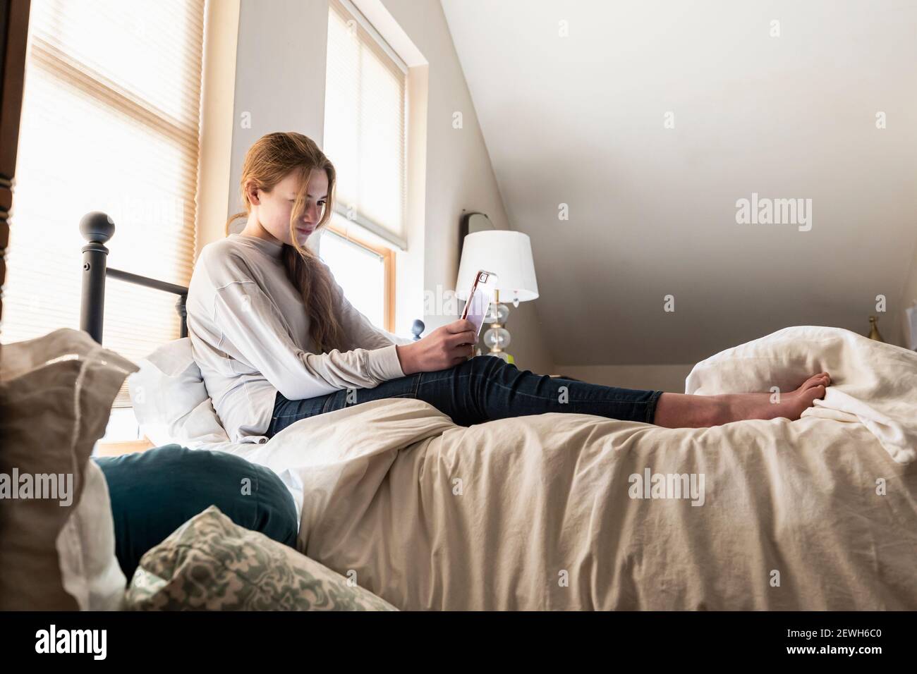 Ragazza adolescente seduta sul suo letto utilizzando il suo smartphone Foto Stock