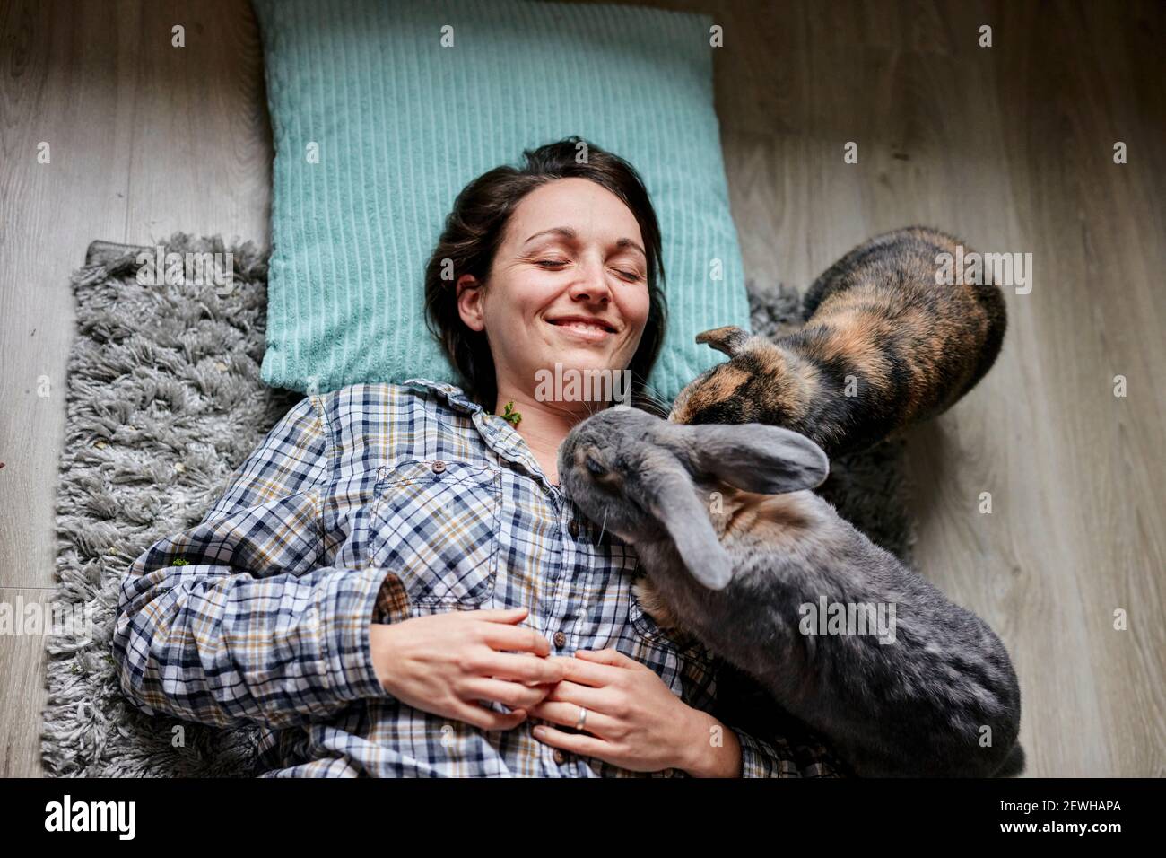 Donna sdraiata sul pavimento circondata da due conigli di casa per animali domestici ripresa dall'alto Foto Stock