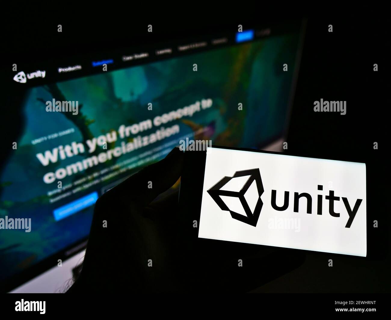 Persona che tiene il telefono cellulare con il logo aziendale della società di videogiochi statunitense Unity Software Inc. Sullo schermo davanti alla pagina web. Mettere a fuoco il display del telefono. Foto Stock